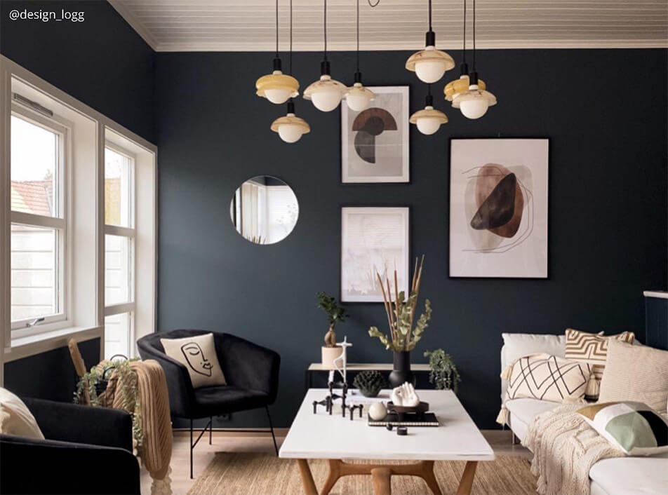 Dnevna soba s temnimi stenami, črnimi kavči iz žametnega materiala, okroglo ogledalo, grafične plakate